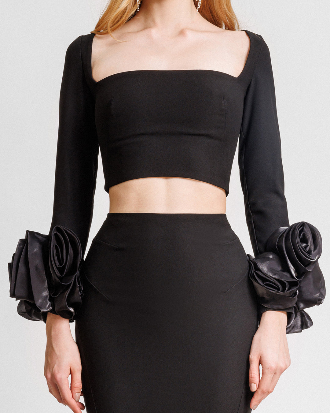 A close-up of an evening wear set featuring a squared-neckline black top with floral cuffs paired with a black skirt.