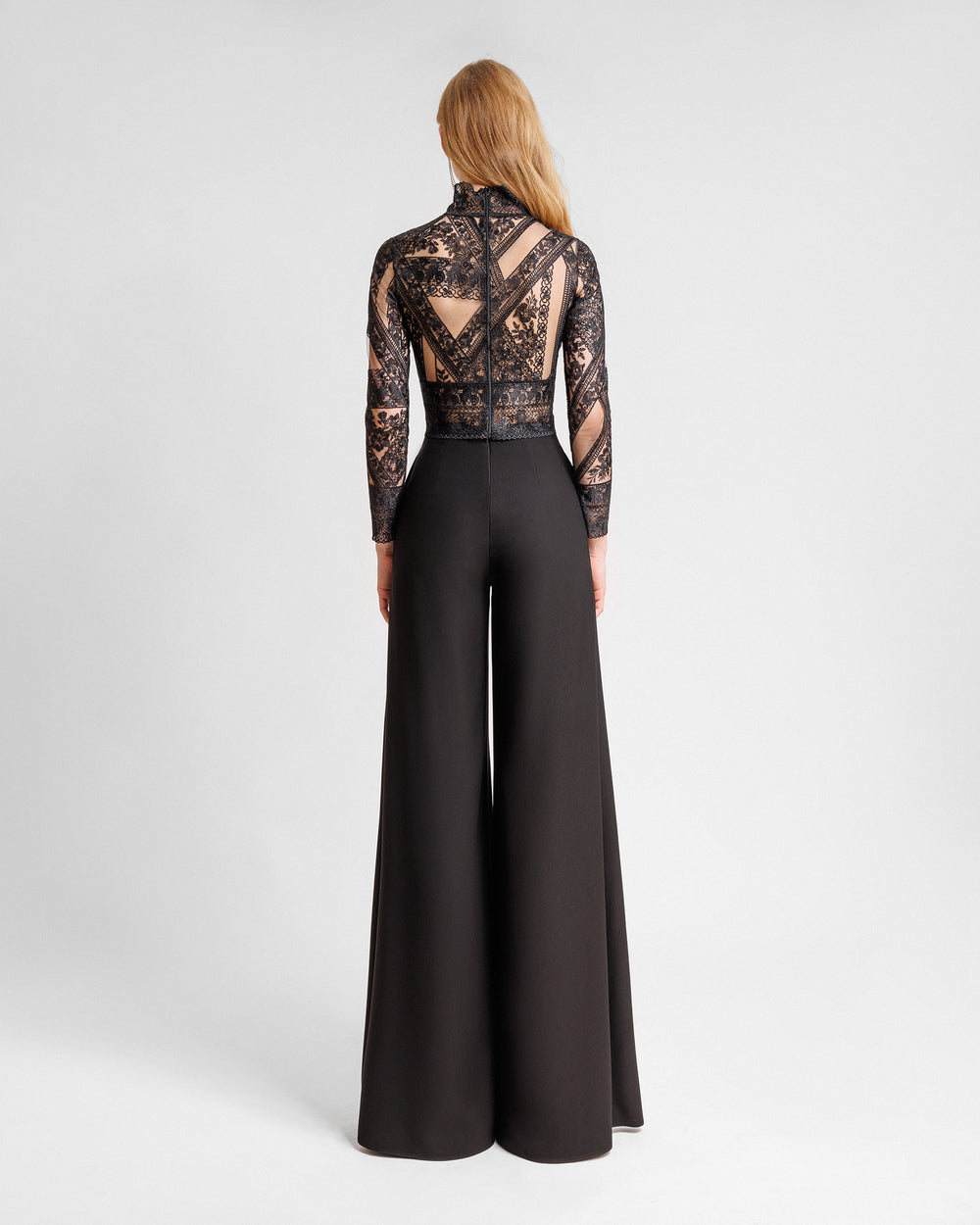 The back of a black evening wear set featuring a long-sleeve patterned lace top paired with straight-cut pants with slits on the sides.