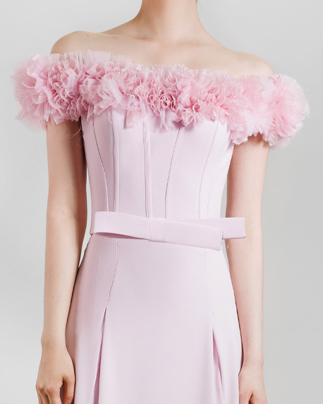 A close-up of a pink occasion wear featuring an off-the-shoulders corset top with rushed details on the neckline paired with a long skirt with openings on the sides.