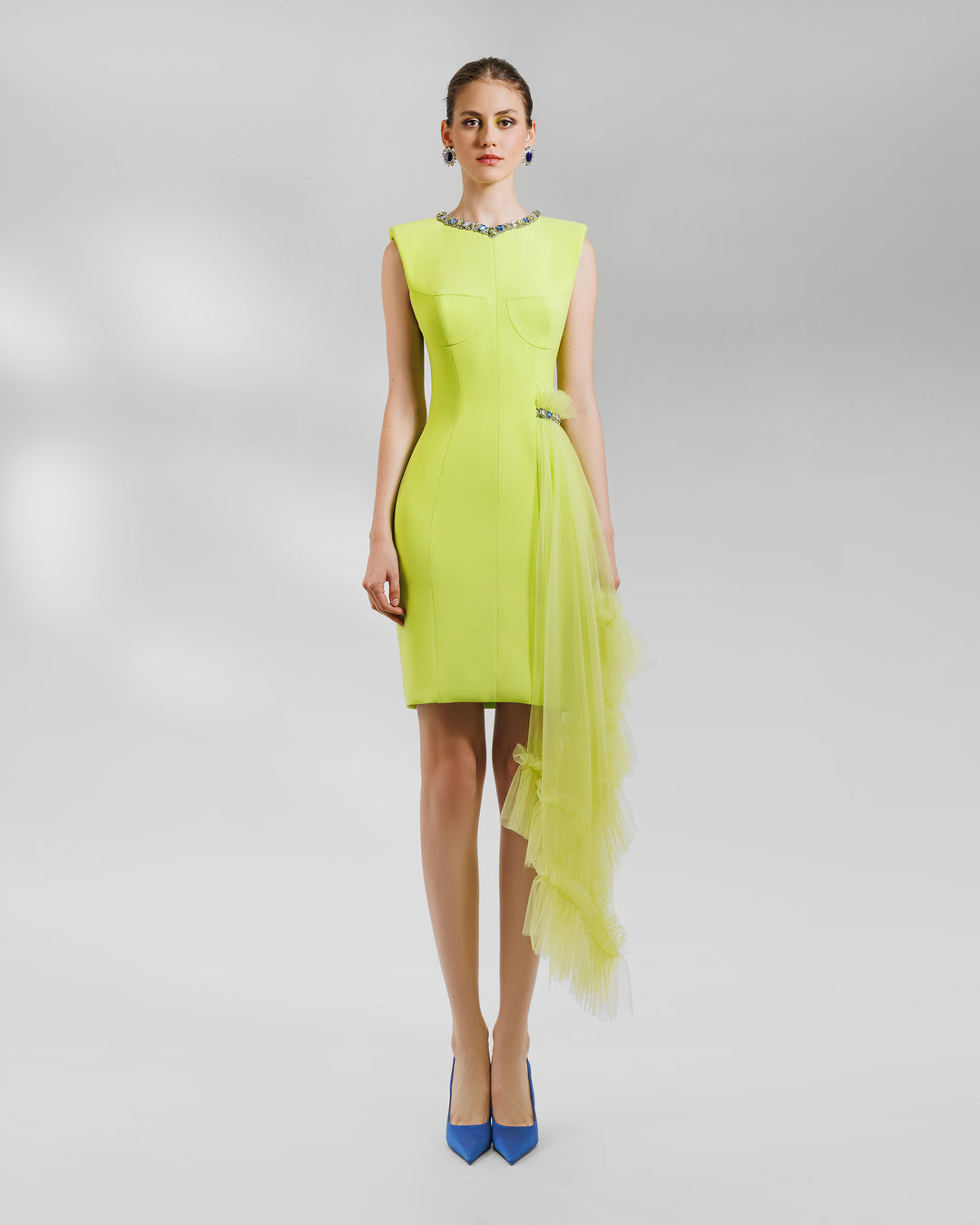 A short structured lime dress with padded shoulders and a round beaded neckline. It features an asymmetrical tulle ruffles on the side with a beaded line.