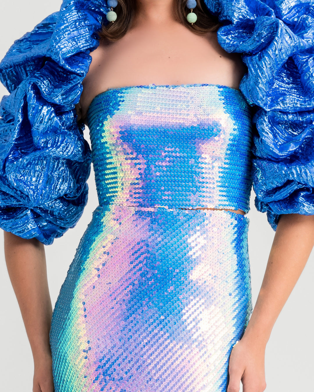 A close-up of an evening wear set featuring a sequined tube top in aqua blue paired with a long skirt and a draped bolero.