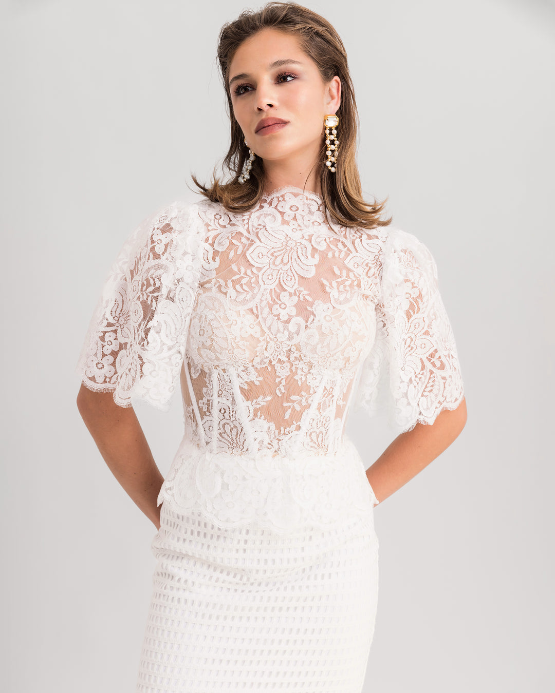 A close-up of a white evening wear set featuring a high-collar lace top with flared sleeves, paired with a midi lace pencil skirt.