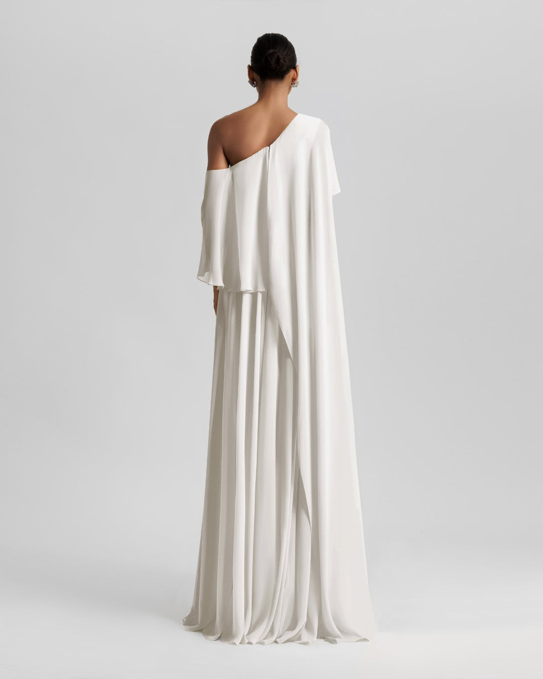 The back of a one-shoulder ivory dress featuring a ruffled cape-like sleeve.