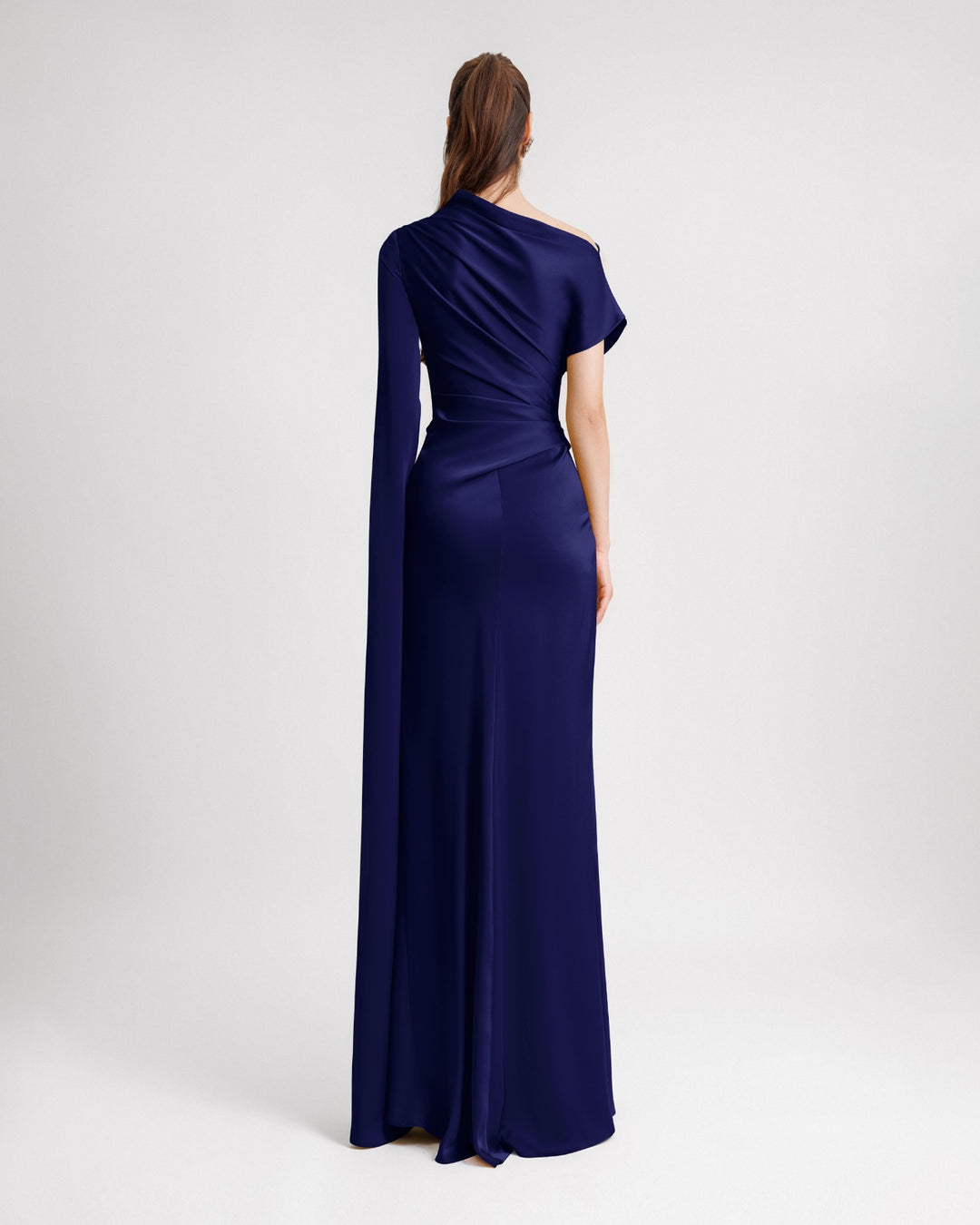 The back of an asymmetrical neckline draped evening dress in navy blue satin fabric with a floor-length sleeve.