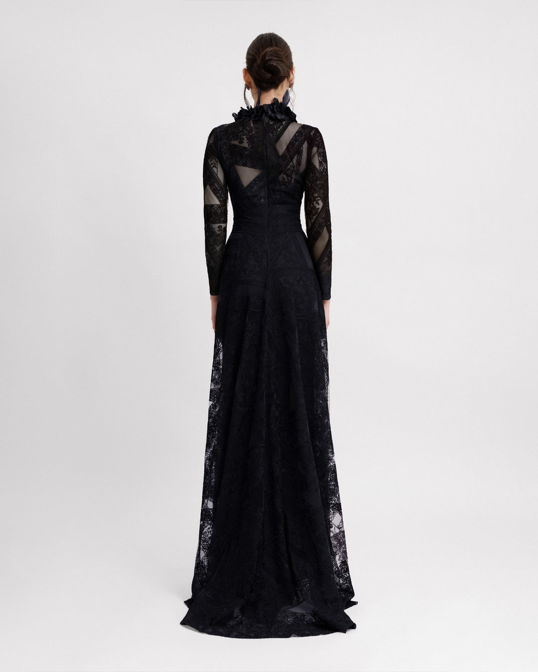 The back of a long sleeved black evening dress in a patterned lace fabric, featuring an embroidered floral feathers on the collar.