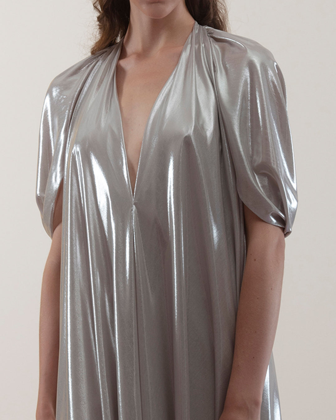 A close-up of a deep V-neckline, loose cut laminated silver chiffon dress.