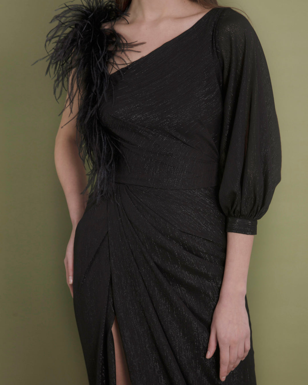 A close-up of an asymmetrical neckline chiffon black evening dress with feather sleeve, draping and open slit on the side.