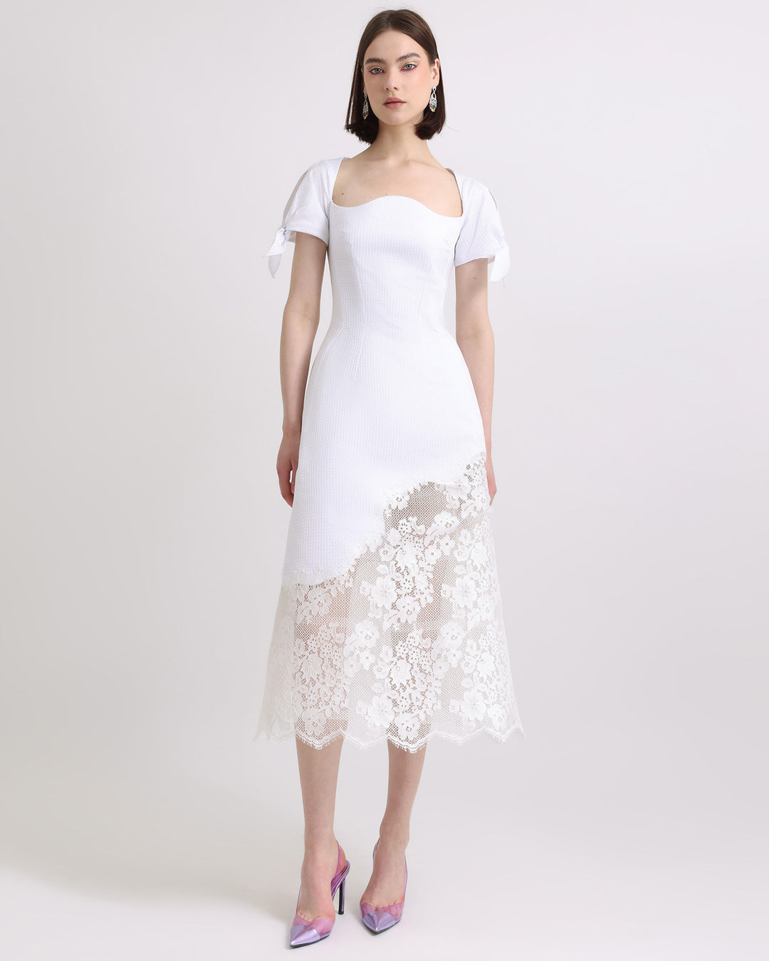 A flared White dress with puffed sleeves and asymmetrical intricate lace on the hemline.