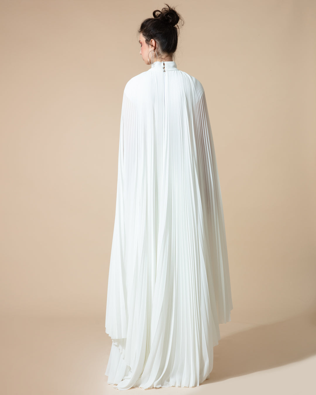 The back of a fully pleated flared chiffon white dress with cape-like asymmetrical sleeves.