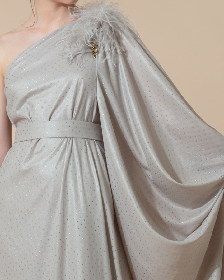 A close-up of a one shoulder long grey evening dress with a draped long sleeve and feathers embellishments on the shoulder line styled with a separate belt.