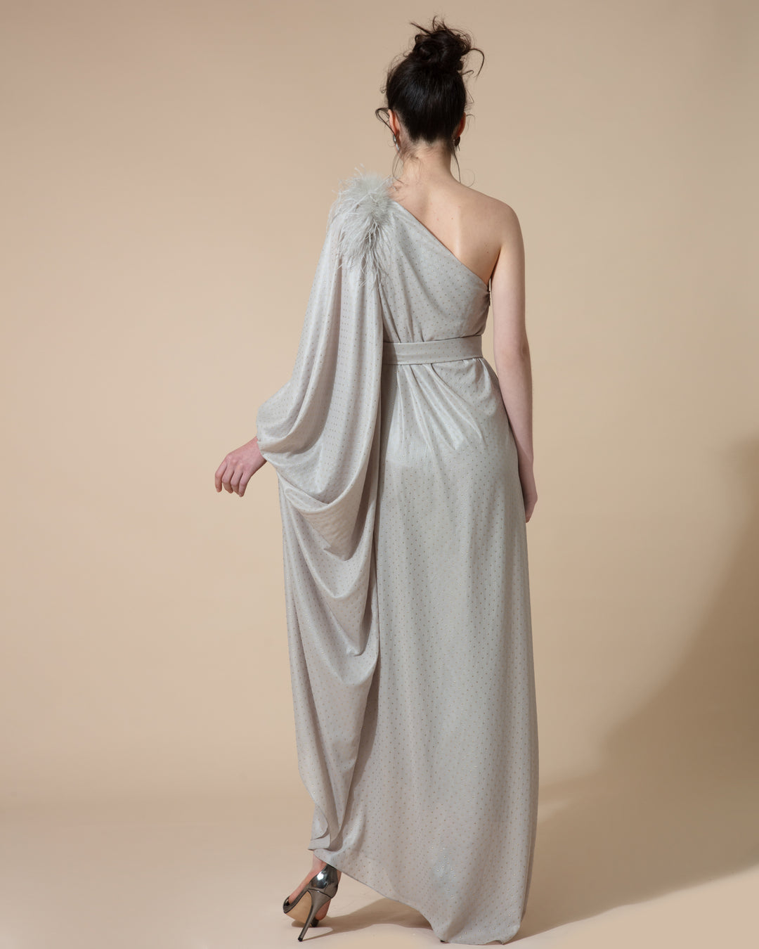 The back of a one shoulder long grey evening dress with a draped long sleeve and feathers embellishments on the shoulder line styled with a separate belt.