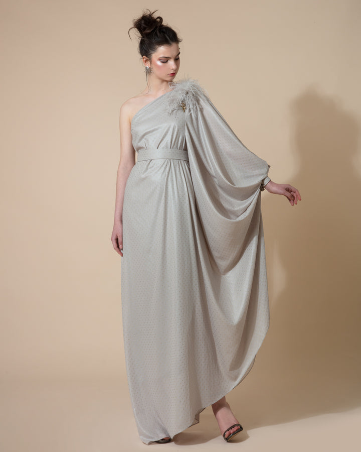 A one shoulder long grey evening dress with a draped long sleeve and feathers embellishments on the shoulder line, styled with a separate belt.