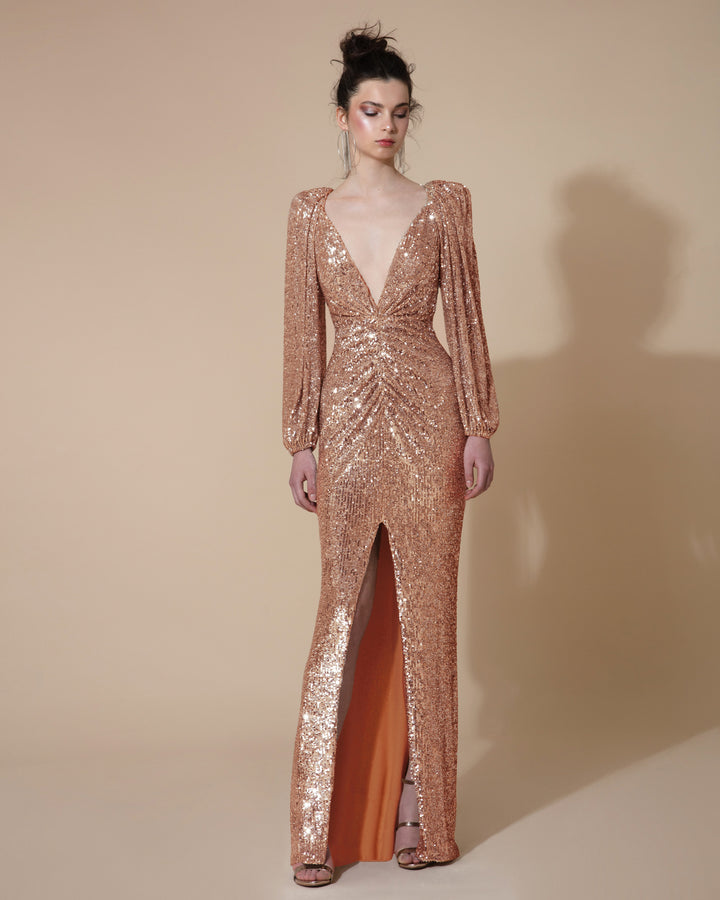 A long evening dress in full copper sequins fabric, featuring a deep V neck, bishop sleeves, gatherings on the waist and a front slit.