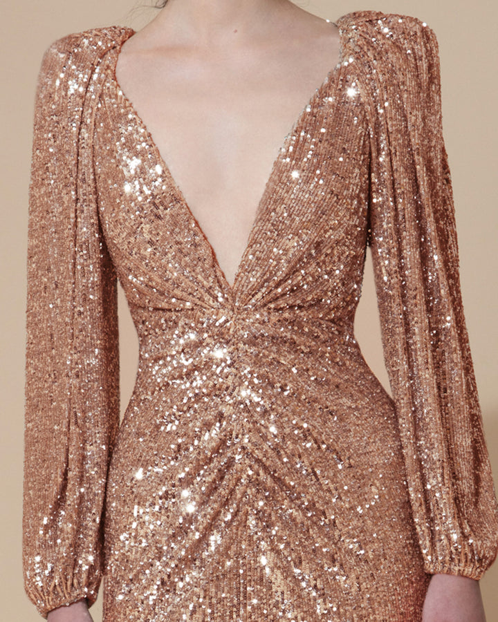 A close-up of a long evening dress in full copper sequins fabric, featuring a deep V neck, bishop sleeves, and gatherings on the waist.