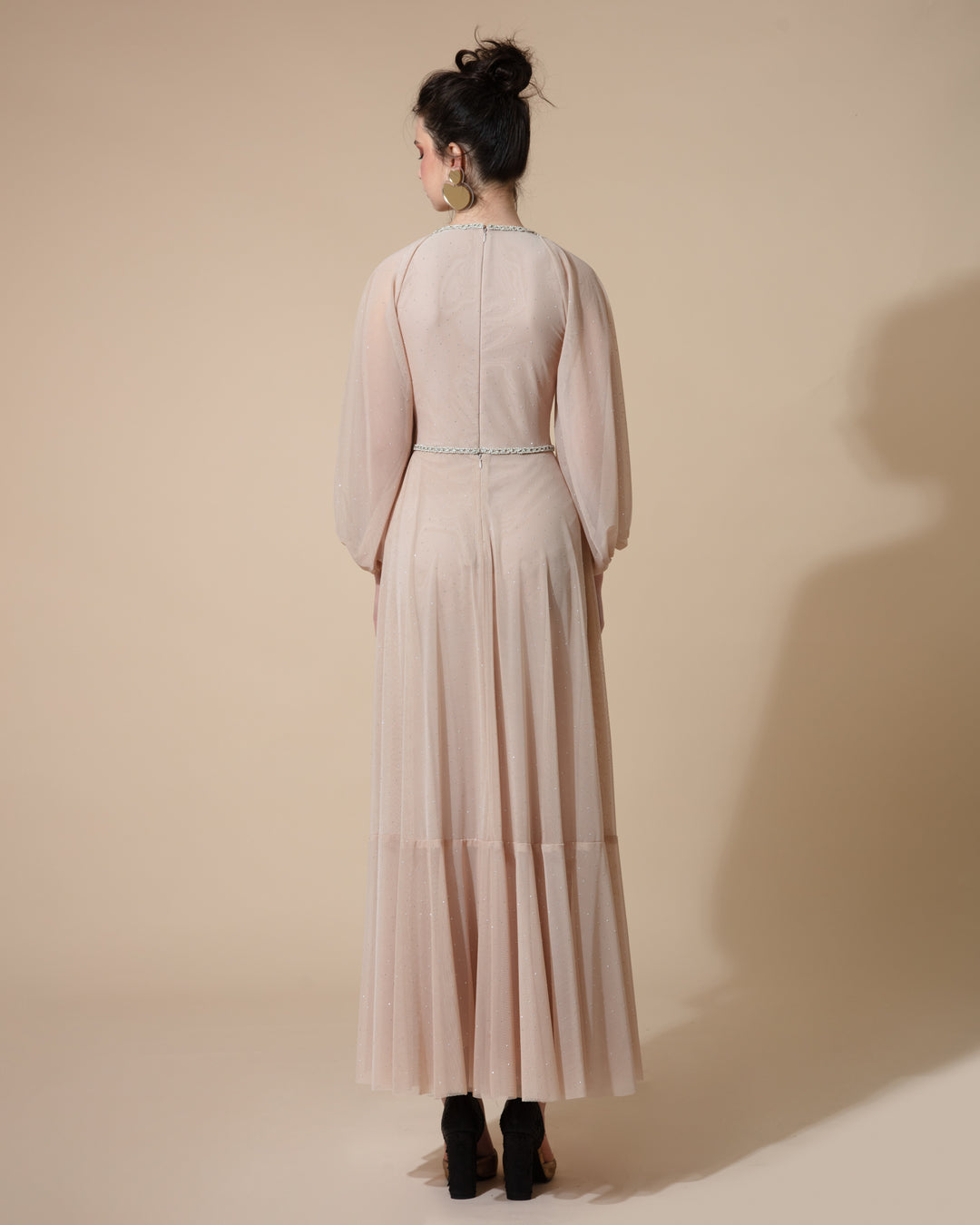 The back of a beige evening dress featuring long raglan sleeves and an embellished belt on the waist.