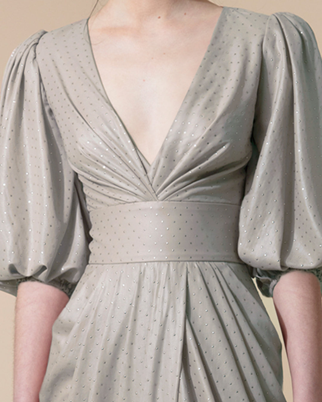 A close-up of a grey evening dress with a deep V neck, short bishop sleeves and a draped skirt.