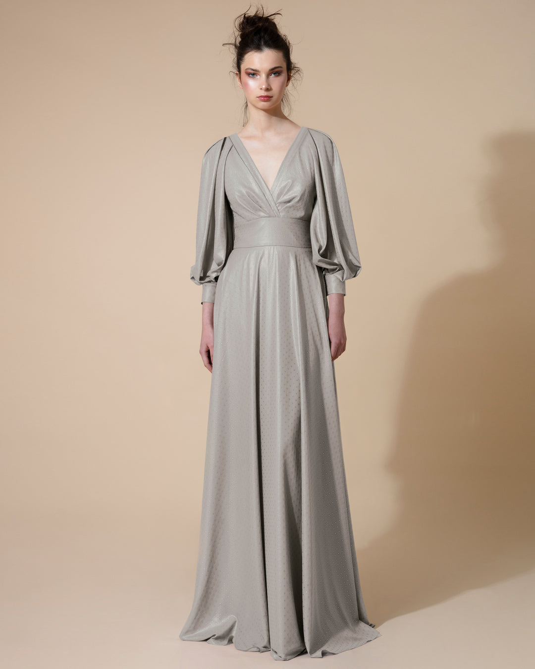 A long silver evening dress with a deep V neck and long bishop sleeves with openings, fitted on the waist.