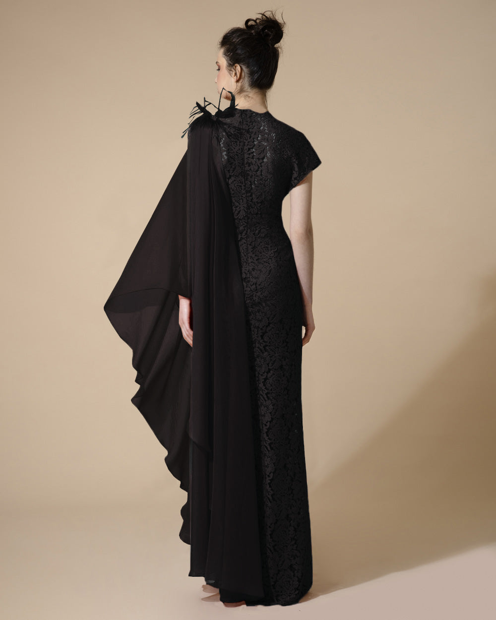 The back of a long fitted black evening dress with short kimono sleeve on one side and draped chiffon sleeve on the other with feathers details.