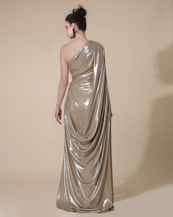 The back of a fully draped long evening dress in metallic gold with a cape-like one sleeve.