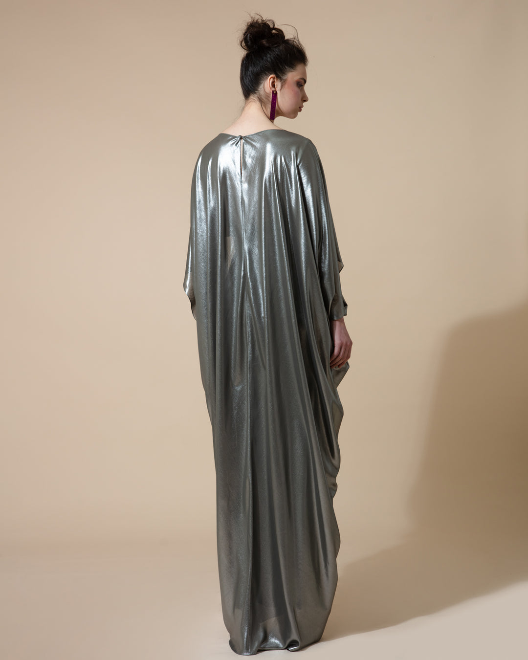 The back of a cape-like long draped evening dress in metallic green.