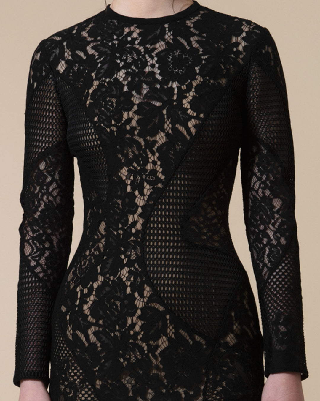 A close-up of a fully lined lace black dress with asymmetrical cuts, long sleeves and a rounded neckline.