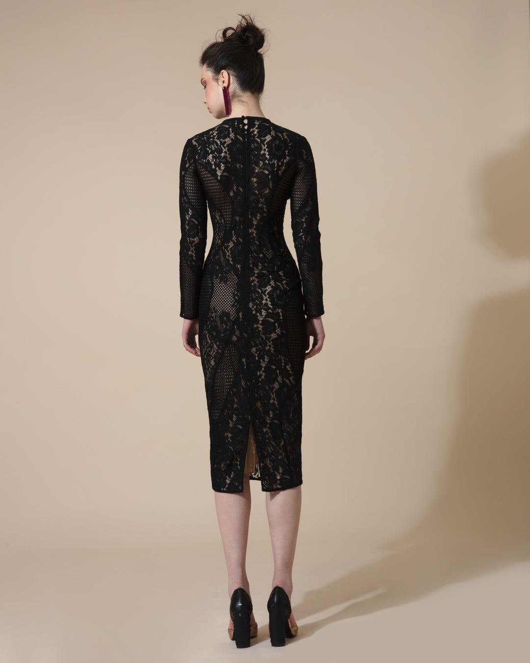 The back of a fully lined lace black dress with asymmetrical cuts, long sleeves and a rounded neckline.