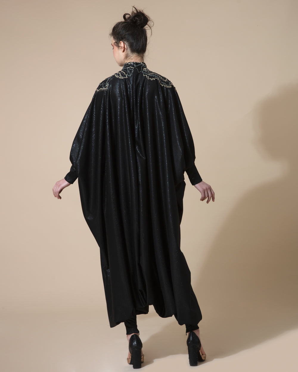 The back of an oversized black jumpsuit with a high neck and embellishments on the neck and shoulders.