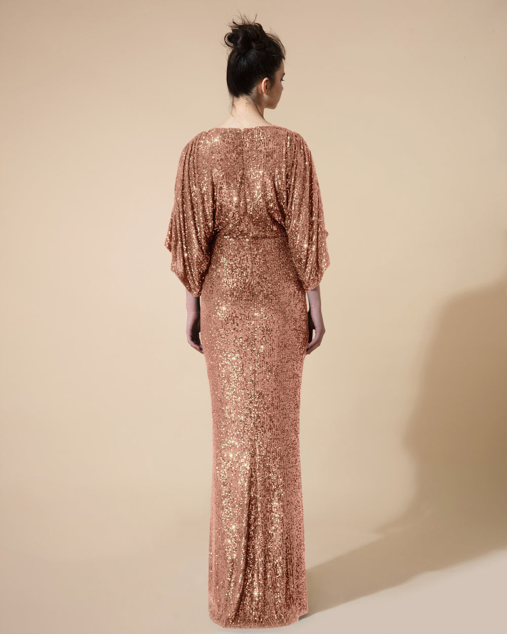 The back of a long fitted evening dress in copper sequins fabric with gathered kimono sleeves.