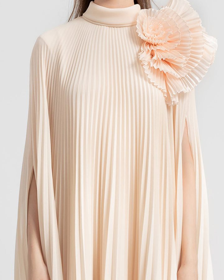 A close-up of a fully pleated lame organza flared beige dress with an embellished draped flower on the shoulder.