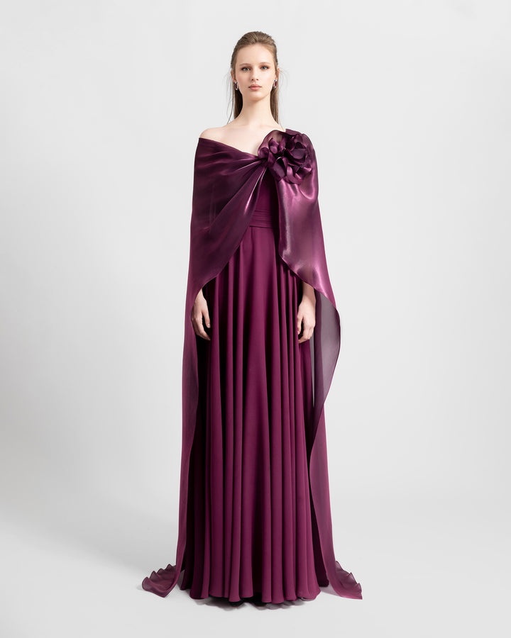 A wide cut neckline with an embellished flower and cape-like sleeves flared soft lame organza evening dress in burgundy color.