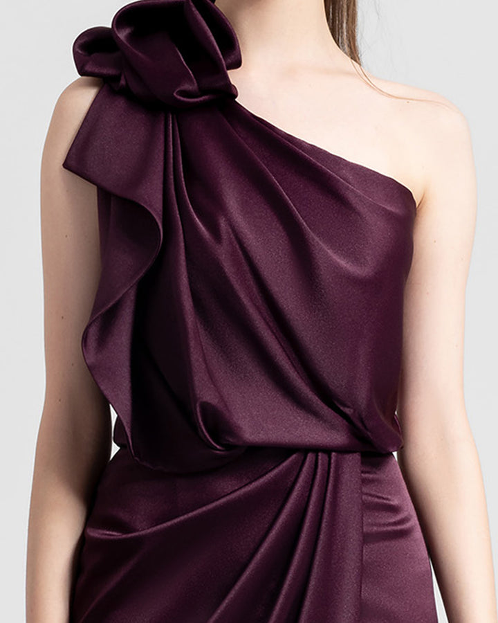 A close-up of a one-shoulder burgundy satin dress with draping details.