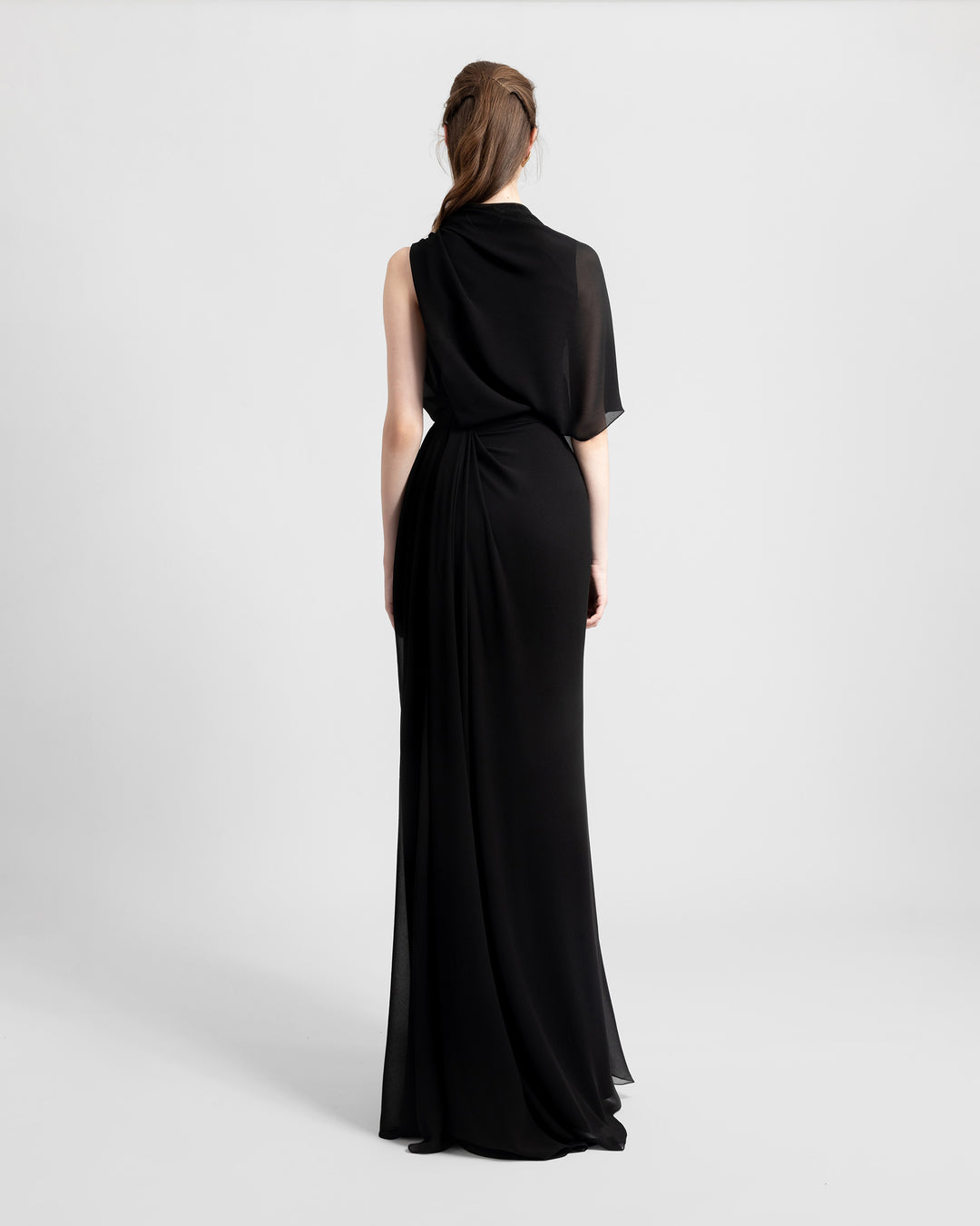 The back of an asymmetrical chiffon black dress with one sleeve and draping details.