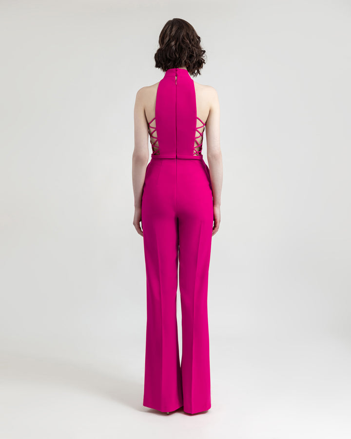 The back of a halter-cut neckline fuchsia jumpsuit with side cut-out details and flared cut pants.