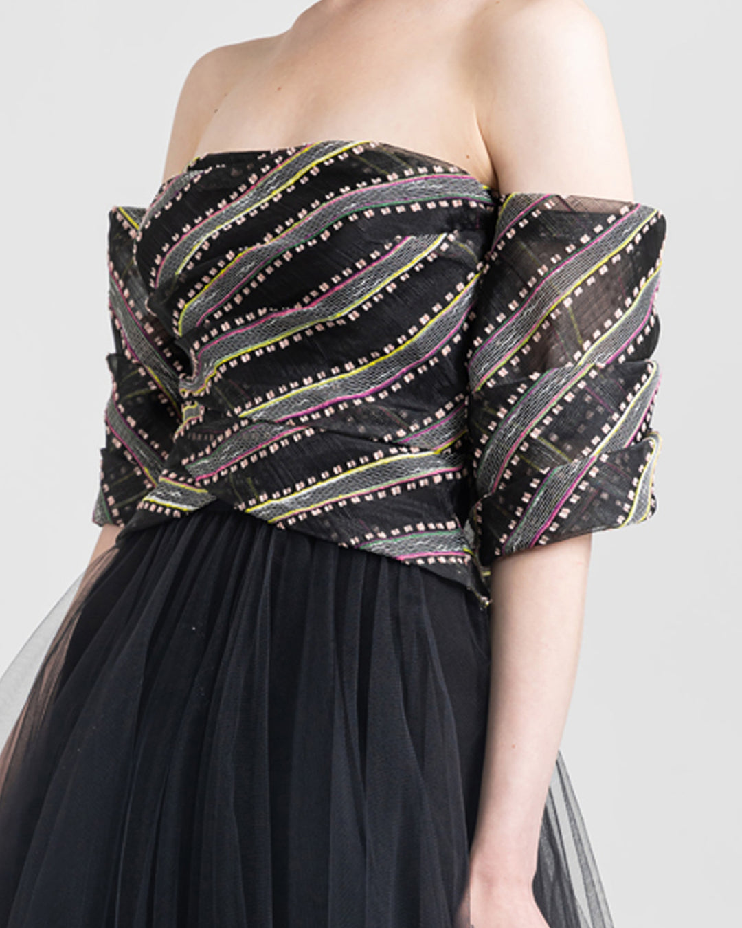 A close-up of an off-the-shoulder evening dress with draping on the bust and a flared black tulle skirt.