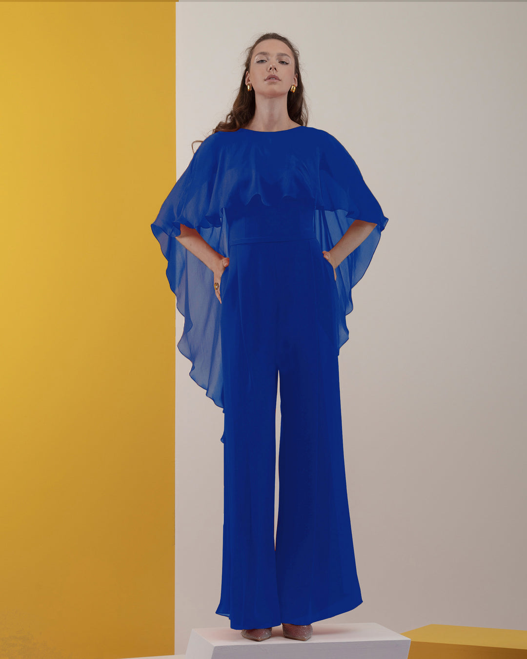 A blue jumpsuit with ruffled flowy chiffon cape-like neckline.