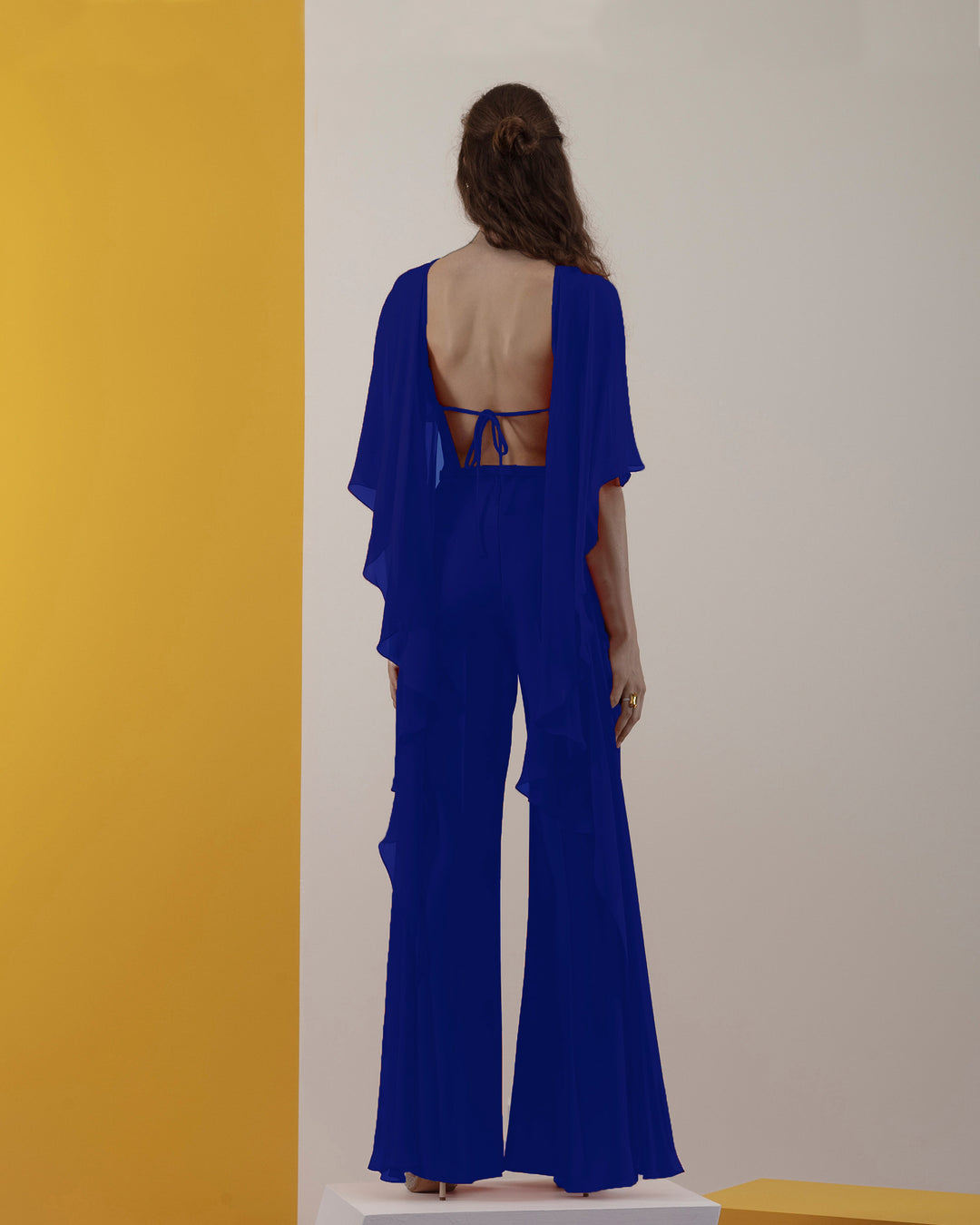 A blue jumpsuit with backless design and ruffled flowy chiffon cape-like neckline.