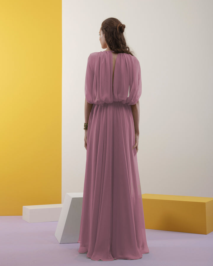 The back of a pink chiffon fabric long evening dress with cape-like sleeves, draped details on the waist, and an open slit on the side.