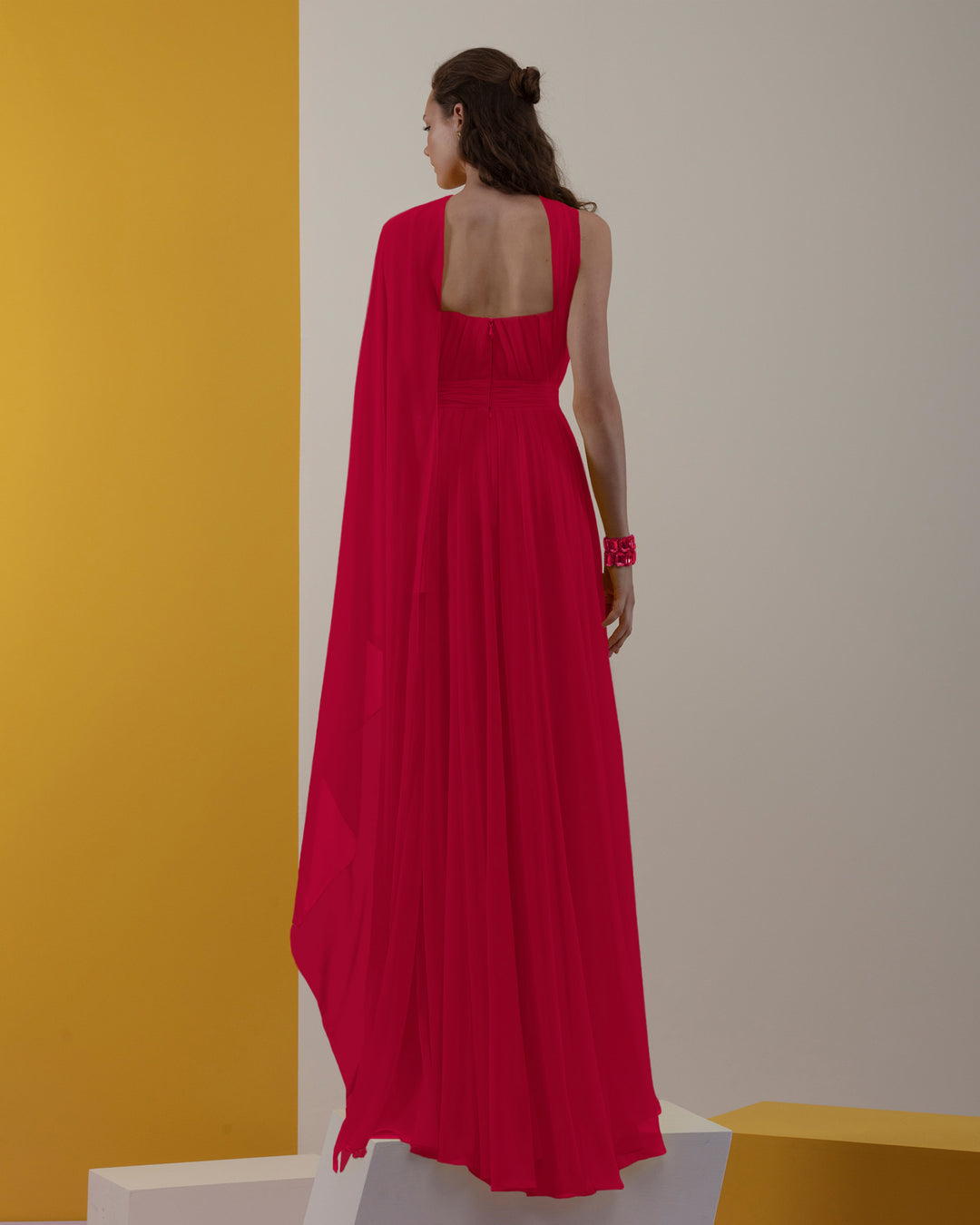 The back of a chiffon red dress with pleating details and one shoulder cape-like flowy design.