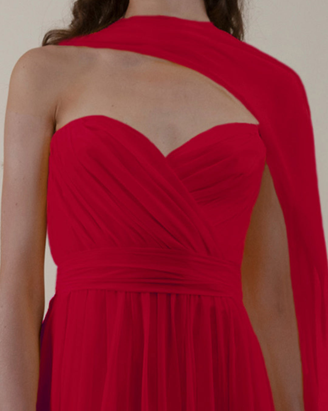 A close-up of a strapless cut, chiffon red dress with pleating details and one shoulder cape-like flowy design.