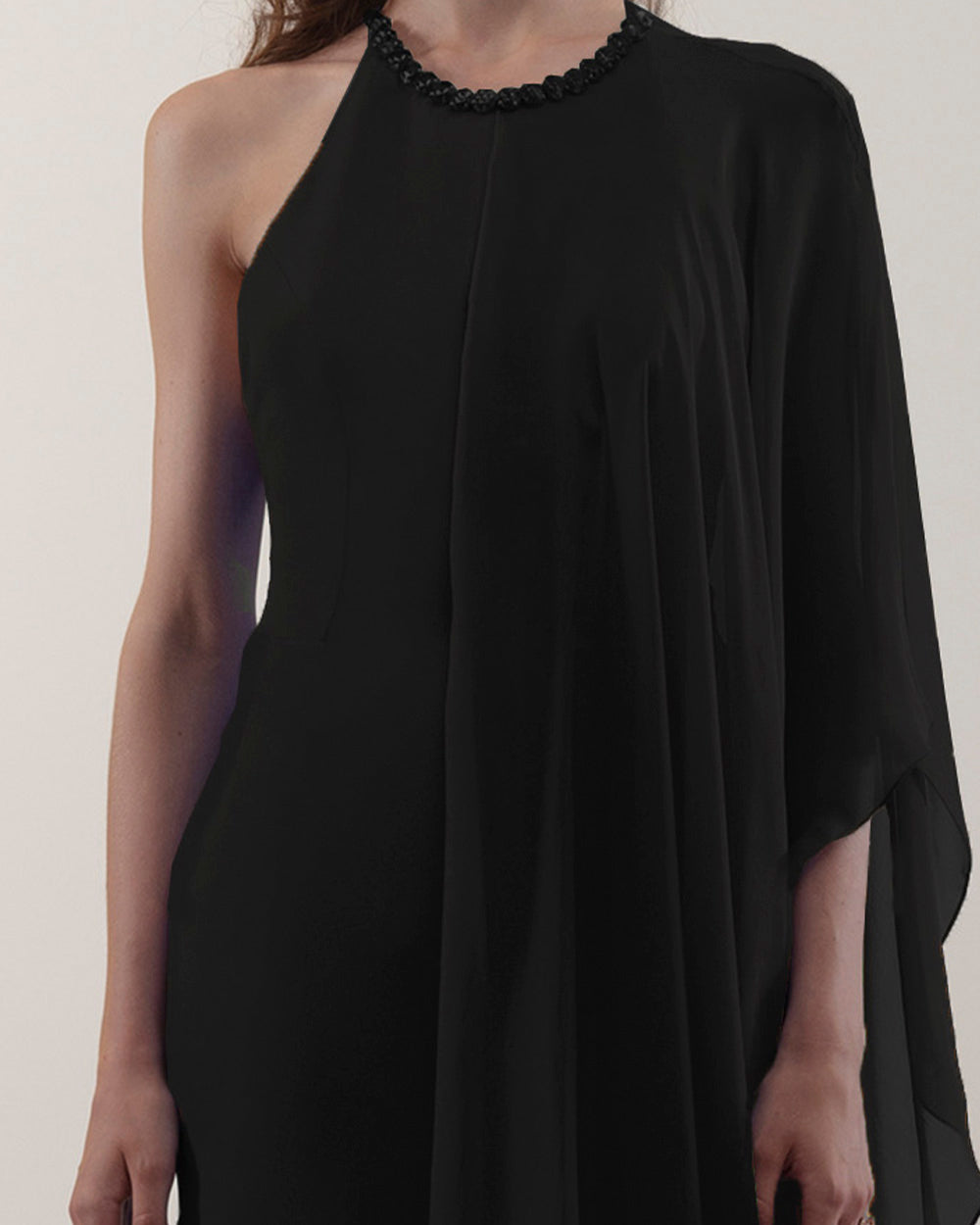 A close-up of a rounded neckline, slim cut crepe black dress with one sided draped flowy chiffon fabric.