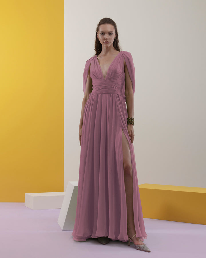 A deep V-neckline, pink chiffon fabric long evening dress with cape-like sleeves, draped details on the waist, and an open slit on the side.