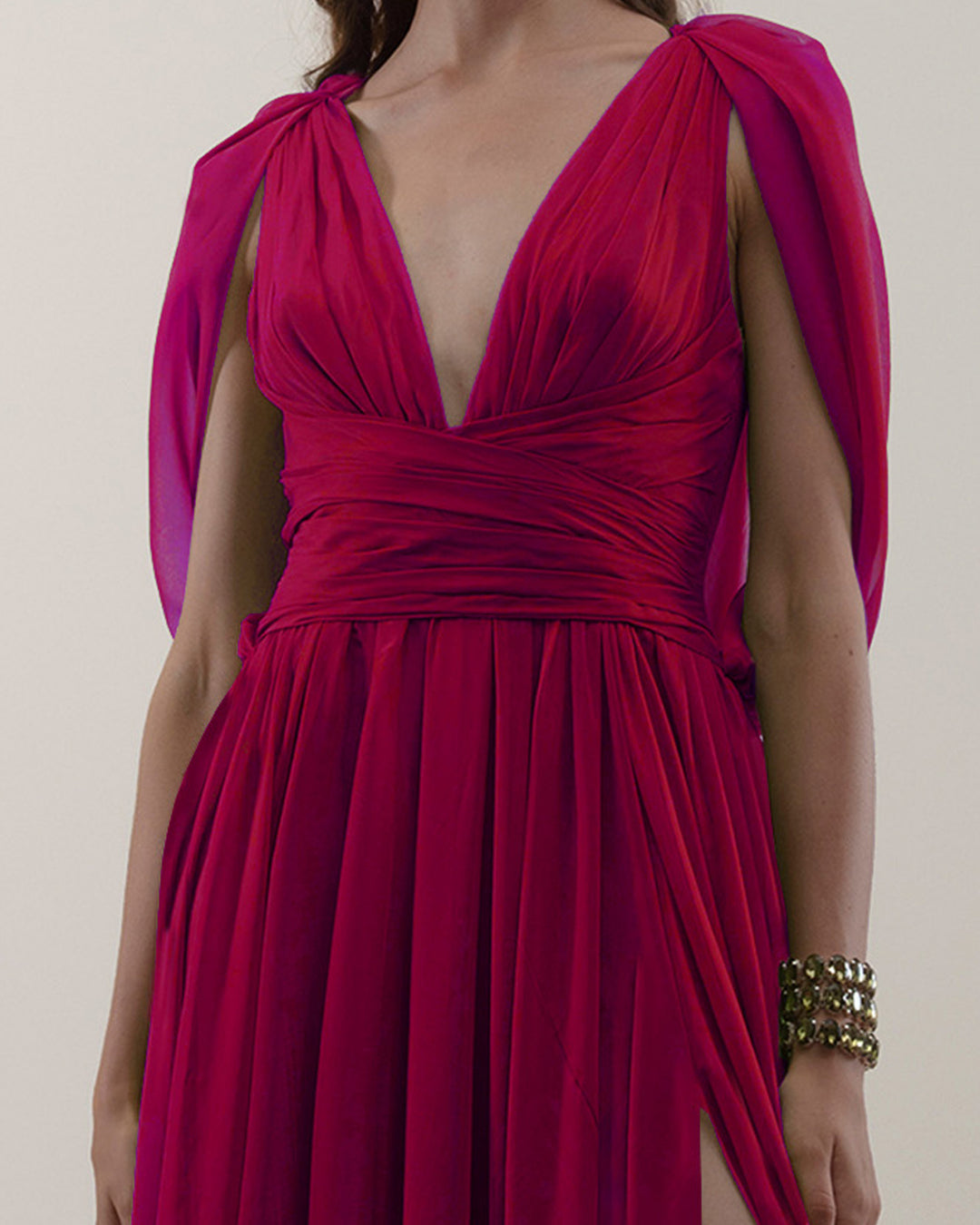 A close-up of a deep V-neckline, chiffon fabric long evening dress with cape-like sleeves, draped details on the waist, and an open slit on the side.