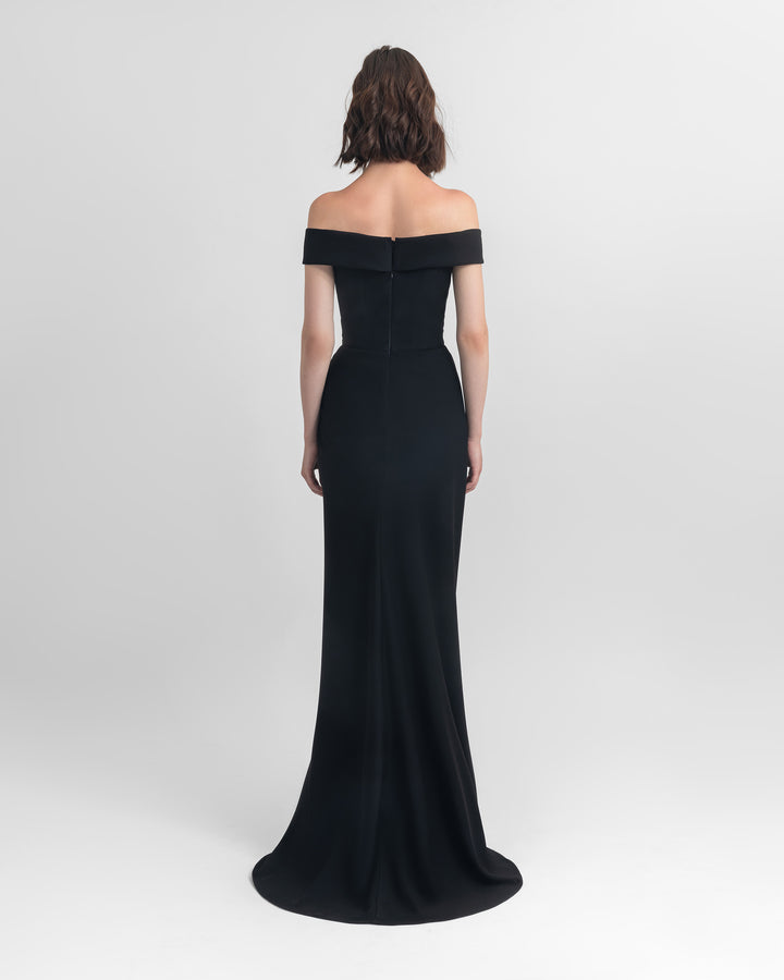 The back of an off-shoulder slim cut crepe long black dress with draping details on the waist and an open slit on the side.