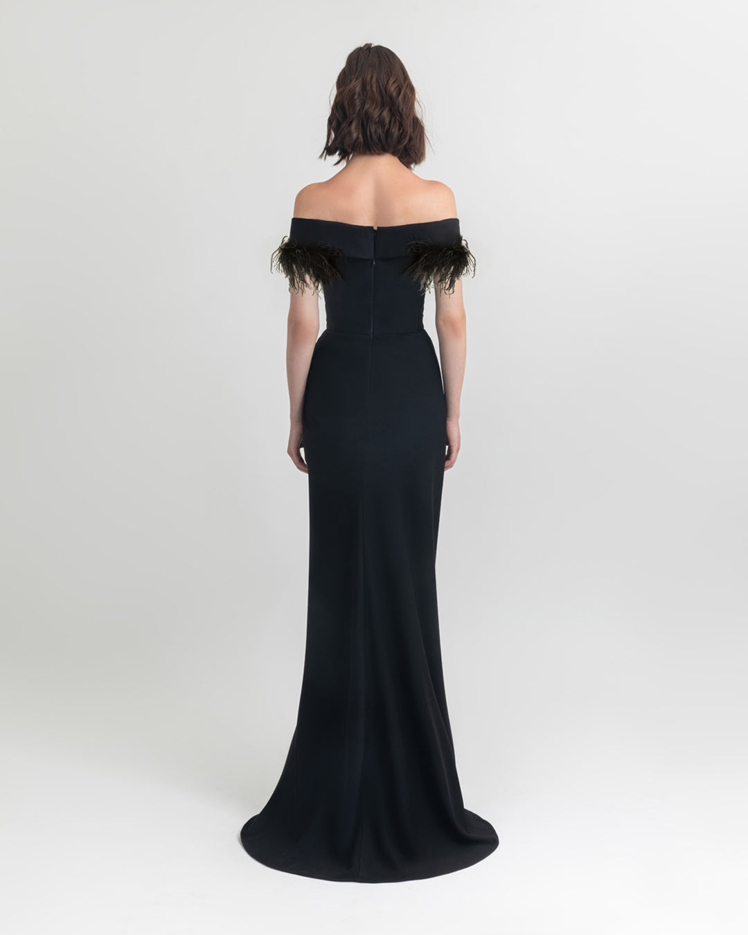 The back of a feathers off shoulder slim cut crepe long black dress.