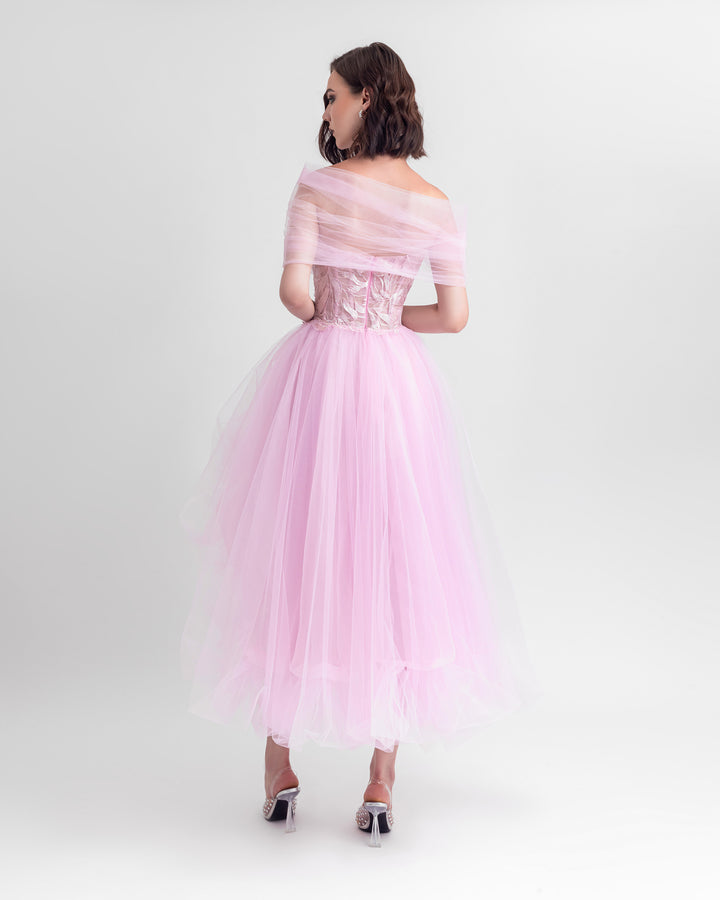 The back of an off-shoulder cut tulle dress in pink with an embroidered corset and an asymmetrical ruffled skirt.