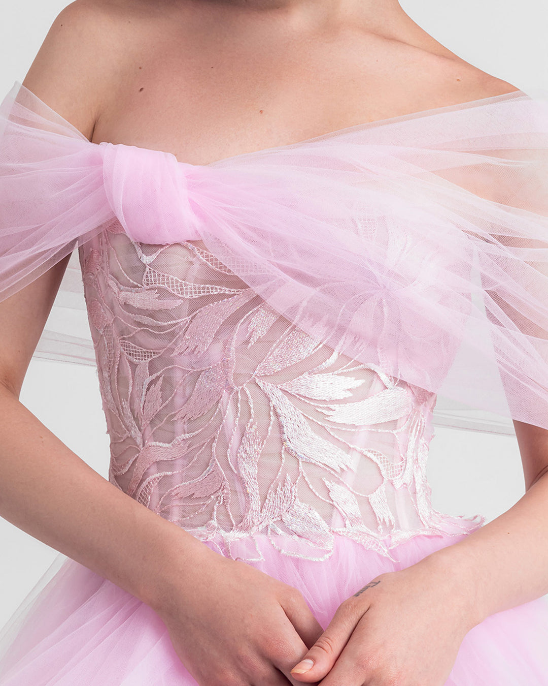 A close-up of a bow-like off-shoulder cut tulle dress in pink with an embroidered corset and an asymmetrical ruffled skirt.