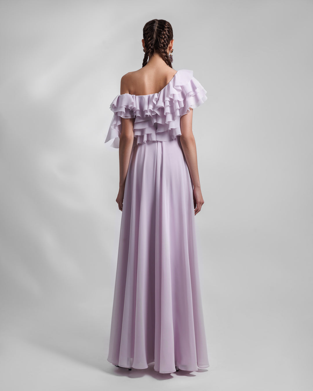 The back of a one-shoulder lilac evening dress in chiffon fabric with ruffled bodice details and an open slit on the side.