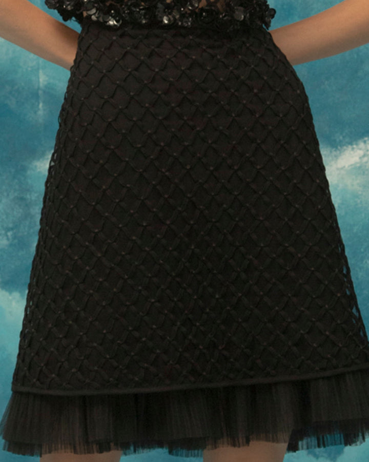 A close-up of a straight cut, embroidered fishnet short black skirt with ruffled details.