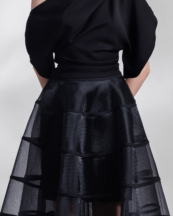 A close-up of a black evening wear set featuring an asymmetrical draped crepe top with slits on the sleeves, matched with a cage-like skirt. 