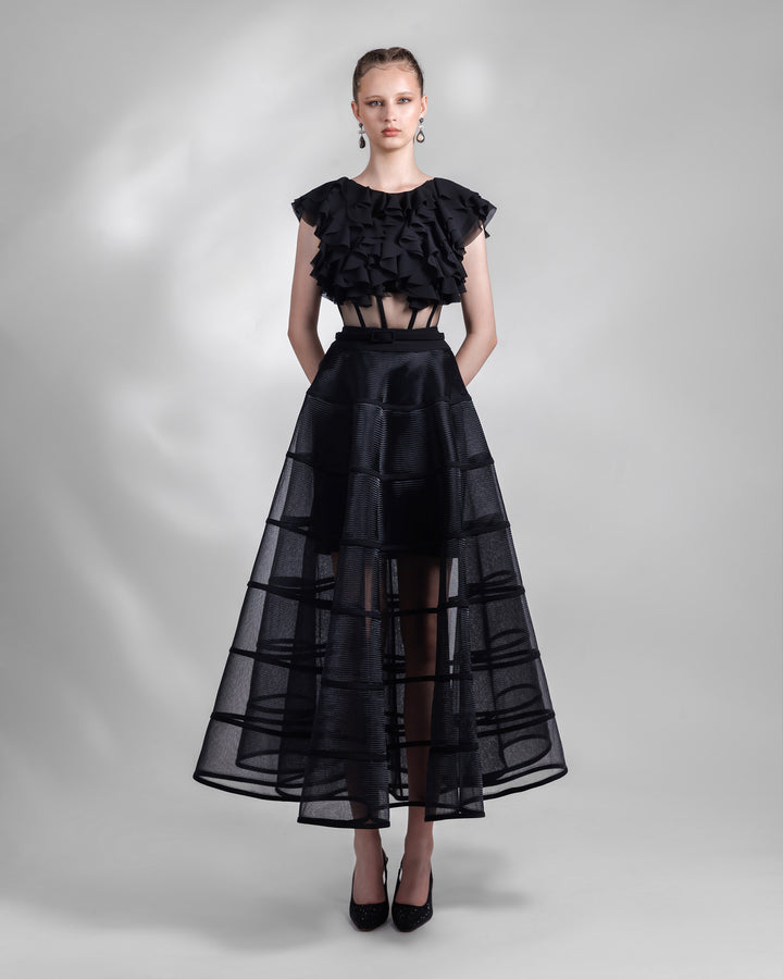 A black evening wear set featuring a ruffled laser cut chiffon top with a see-through corseted bodice paired with a cage like long skirt.